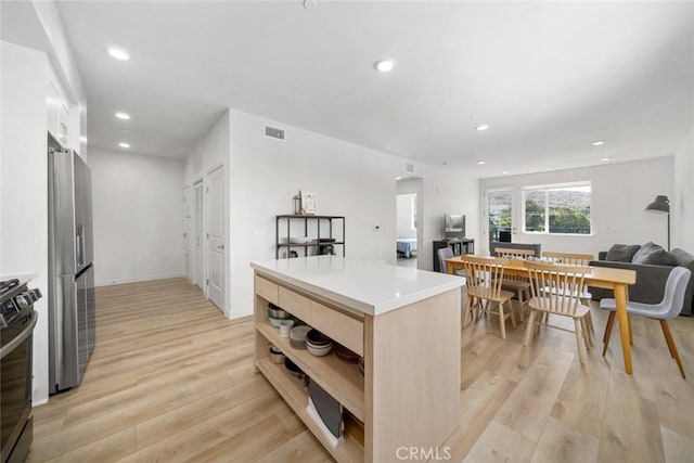 kitchen with appliances with stainless steel finishes, light brown cabinets, light hardwood / wood-style floors, and a kitchen island