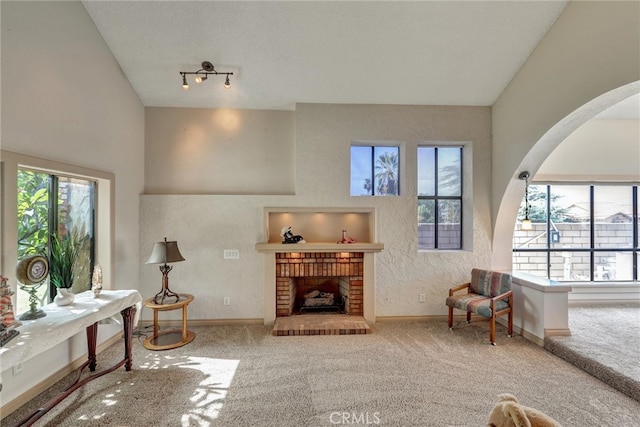 living area featuring vaulted ceiling, carpet flooring, a brick fireplace, and plenty of natural light