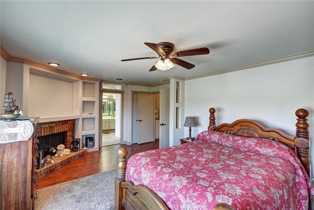 bedroom with wood-type flooring, ensuite bath, crown molding, a brick fireplace, and ceiling fan