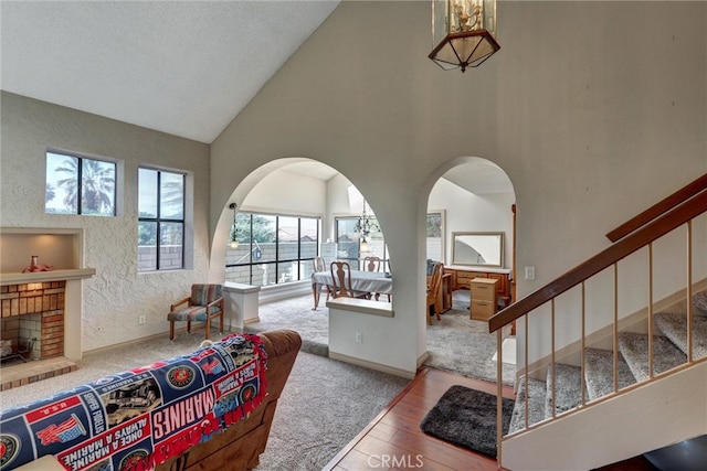 living room with high vaulted ceiling, a brick fireplace, and hardwood / wood-style floors