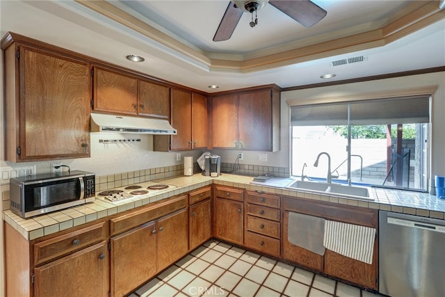 kitchen with appliances with stainless steel finishes, a tray ceiling, crown molding, tile counters, and sink