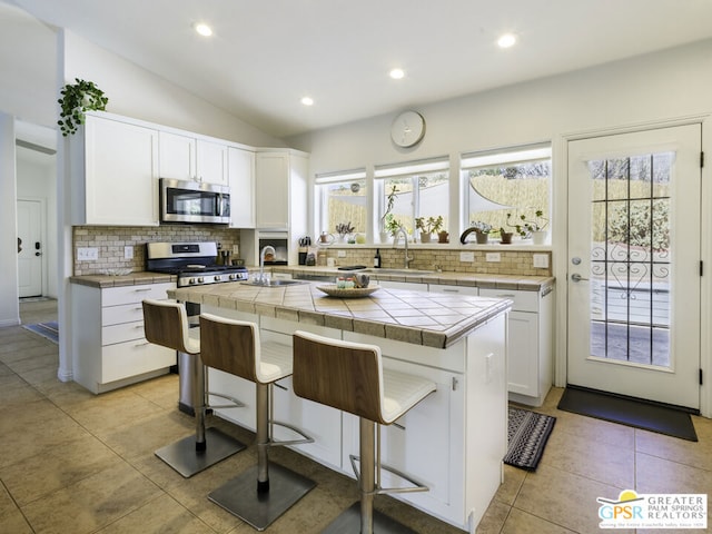 kitchen featuring a center island, white cabinets, a kitchen bar, stainless steel appliances, and tile countertops