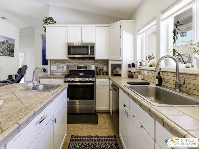 kitchen with tile counters, sink, stainless steel appliances, and a wealth of natural light