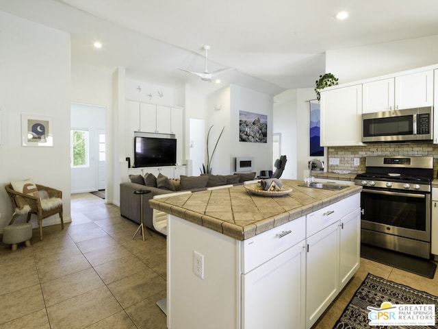 kitchen featuring appliances with stainless steel finishes, decorative backsplash, white cabinetry, an island with sink, and sink