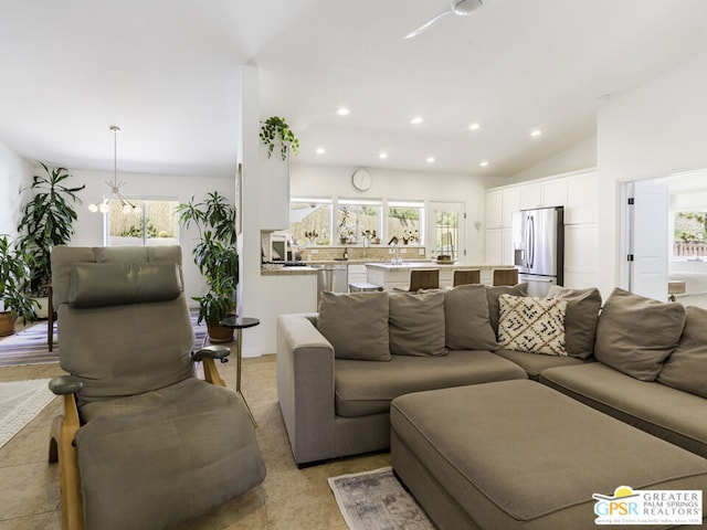 living room with a notable chandelier, vaulted ceiling, light tile patterned floors, and a healthy amount of sunlight