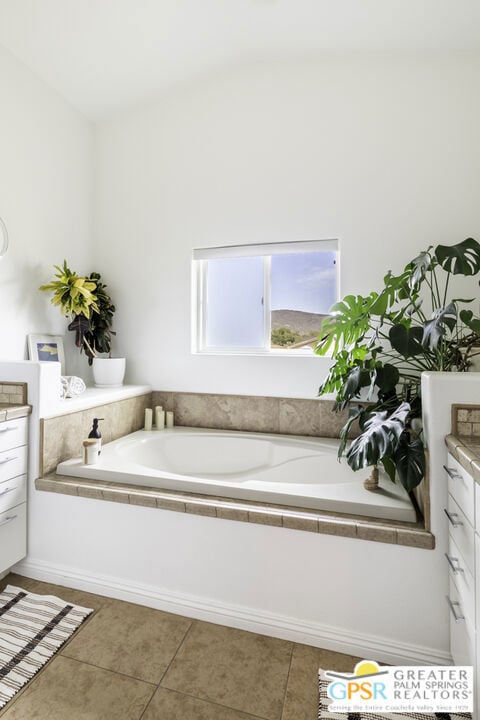 bathroom with a relaxing tiled tub, vanity, and tile patterned flooring