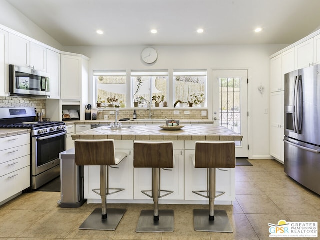 kitchen with a breakfast bar, stainless steel appliances, a center island, and tile countertops