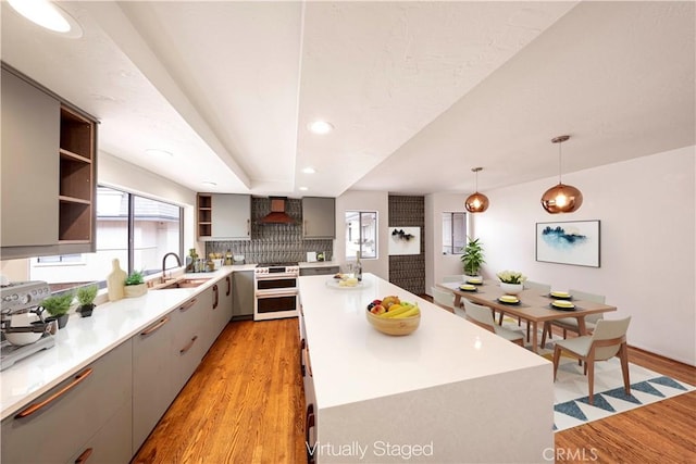 kitchen with hanging light fixtures, high end stainless steel range oven, a kitchen island, custom range hood, and light wood-type flooring