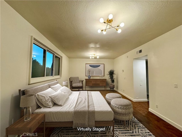 bedroom featuring a textured ceiling, dark wood-type flooring, and an inviting chandelier