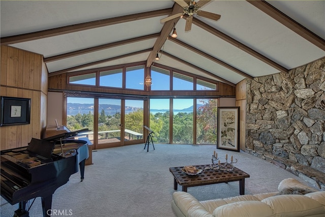 carpeted living room with high vaulted ceiling, wood walls, ceiling fan, and a healthy amount of sunlight