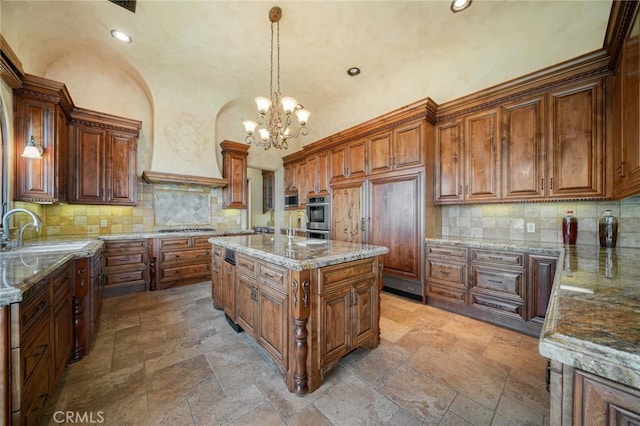 kitchen with backsplash, a kitchen island with sink, sink, decorative light fixtures, and a chandelier