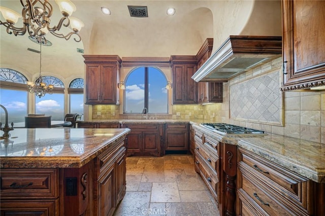 kitchen featuring light stone countertops, pendant lighting, a center island, and an inviting chandelier