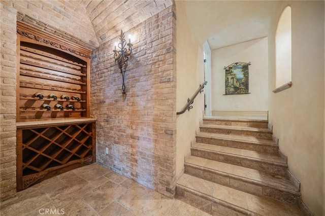 wine area with vaulted ceiling, brick ceiling, and brick wall