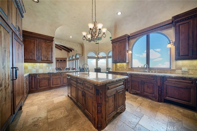 kitchen with a chandelier, a kitchen island with sink, tasteful backsplash, and pendant lighting