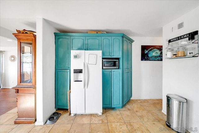 kitchen featuring blue cabinetry, white fridge with ice dispenser, stainless steel microwave, and light tile patterned floors