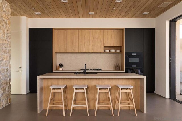 kitchen with a kitchen island with sink, sink, tasteful backsplash, and wooden ceiling