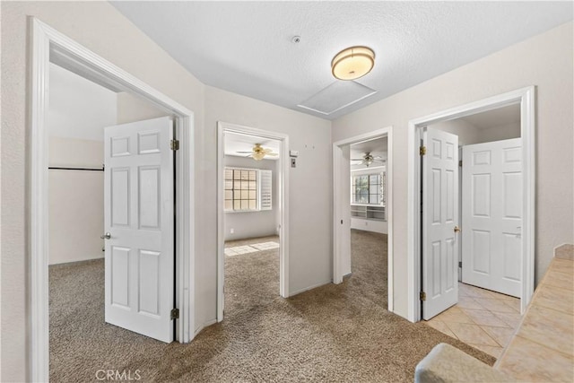 corridor featuring attic access, a textured ceiling, and carpet flooring
