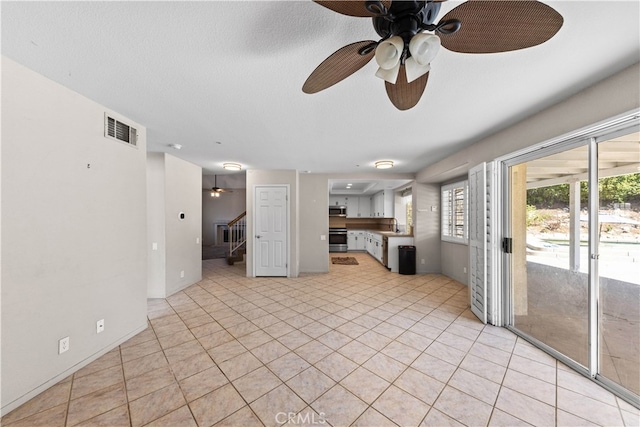 unfurnished living room with ceiling fan, a textured ceiling, and light tile patterned floors