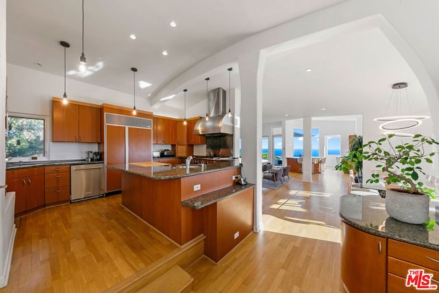 kitchen featuring wall chimney range hood, stainless steel dishwasher, paneled built in refrigerator, decorative light fixtures, and light wood-type flooring