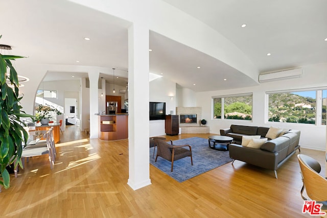 living room with vaulted ceiling, light hardwood / wood-style flooring, and an AC wall unit