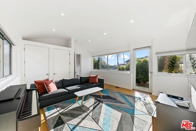 living room with a healthy amount of sunlight, light hardwood / wood-style flooring, and vaulted ceiling