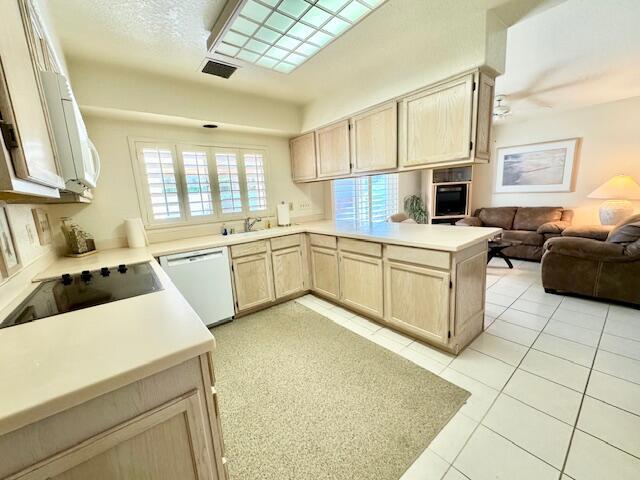 kitchen with black appliances, kitchen peninsula, light tile patterned flooring, and light brown cabinetry