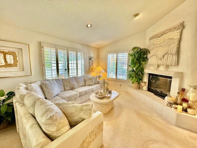 living room with a textured ceiling, lofted ceiling, carpet flooring, and a tiled fireplace