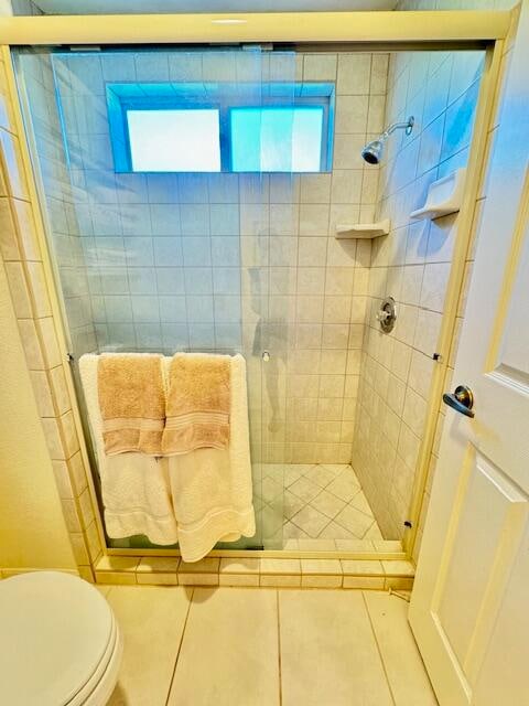 bathroom with a shower with shower door, toilet, and tile patterned flooring