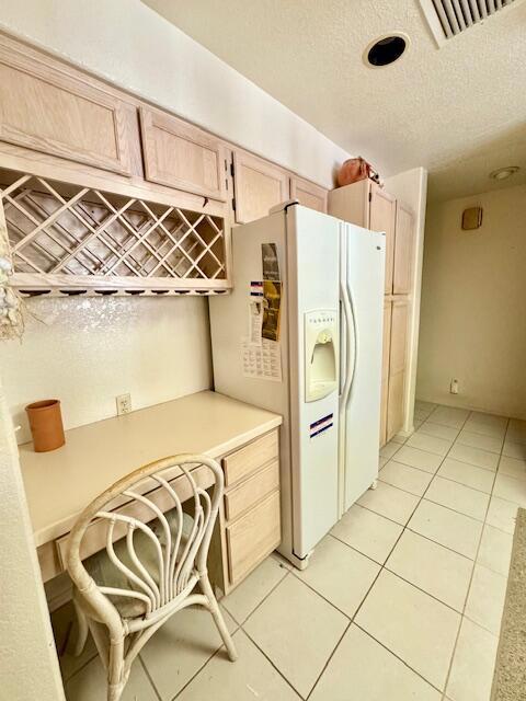 kitchen featuring a textured ceiling, white fridge with ice dispenser, light brown cabinetry, and light tile patterned floors