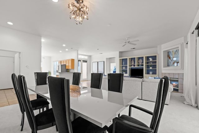 dining area with a tiled fireplace, light tile patterned floors, and ceiling fan with notable chandelier