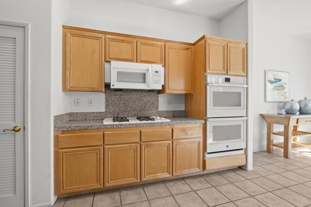 kitchen featuring tasteful backsplash, light tile patterned flooring, and white appliances