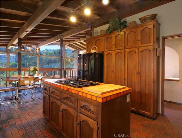 kitchen featuring a center island, stainless steel gas stovetop, track lighting, lofted ceiling, and black fridge with ice dispenser