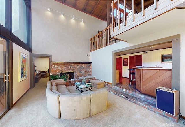 living room with a towering ceiling, track lighting, a brick fireplace, wood ceiling, and carpet floors