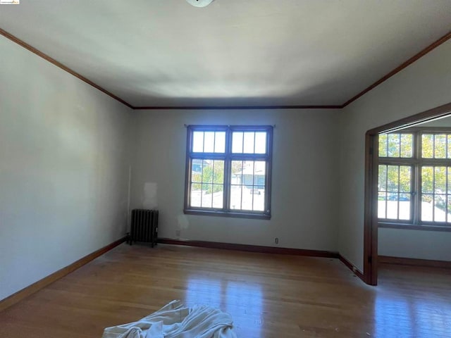 unfurnished room featuring light wood-type flooring, a healthy amount of sunlight, crown molding, and radiator heating unit