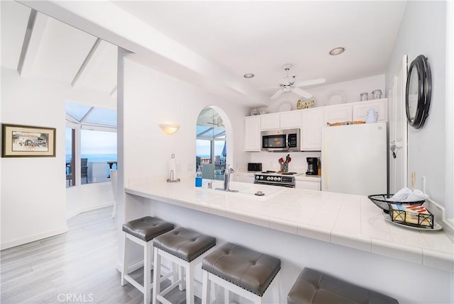 42 Camino De Flores Unit 60, Avalon, CA 90704 - kitchen with stainless steel microwave, electric range oven, a peninsula, white cabinetry, and freestanding refrigerator