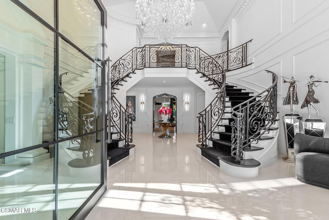 foyer with crown molding, a towering ceiling, and an inviting chandelier