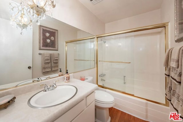 full bathroom featuring a chandelier, wood-type flooring, toilet, shower / bath combination with glass door, and vanity