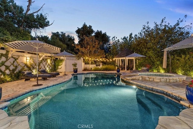 pool at dusk featuring an in ground hot tub and a patio