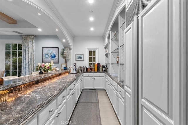 kitchen featuring kitchen peninsula, light wood-type flooring, dark stone counters, sink, and white cabinetry