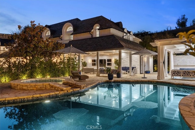 pool at dusk with an in ground hot tub and a patio