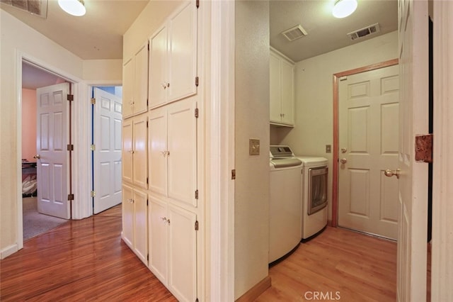 laundry area with cabinets, light hardwood / wood-style floors, and washing machine and clothes dryer