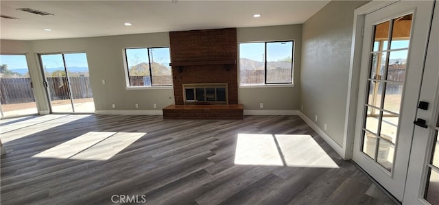 unfurnished living room with a brick fireplace, dark hardwood / wood-style flooring, and a wealth of natural light