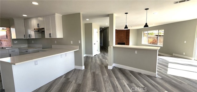 kitchen with wood-type flooring, white cabinets, kitchen peninsula, a kitchen bar, and decorative light fixtures