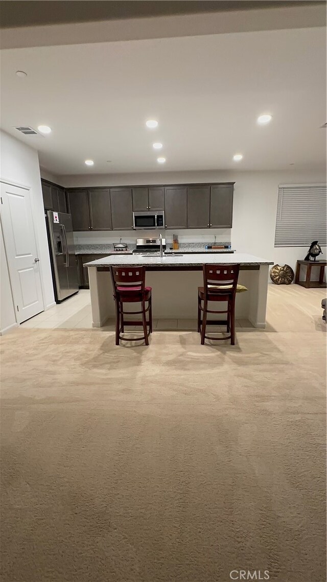 kitchen with light carpet, an island with sink, a kitchen bar, and stainless steel appliances