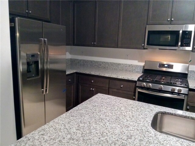 kitchen with appliances with stainless steel finishes, light stone counters, and dark brown cabinets