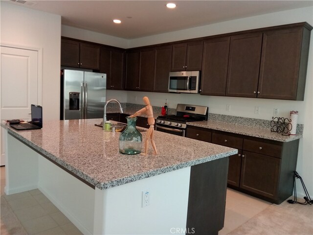 kitchen featuring sink, light stone counters, stainless steel appliances, and dark brown cabinets