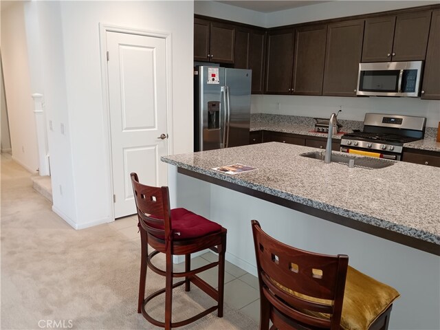 kitchen featuring light carpet, dark brown cabinets, a breakfast bar area, appliances with stainless steel finishes, and light stone countertops