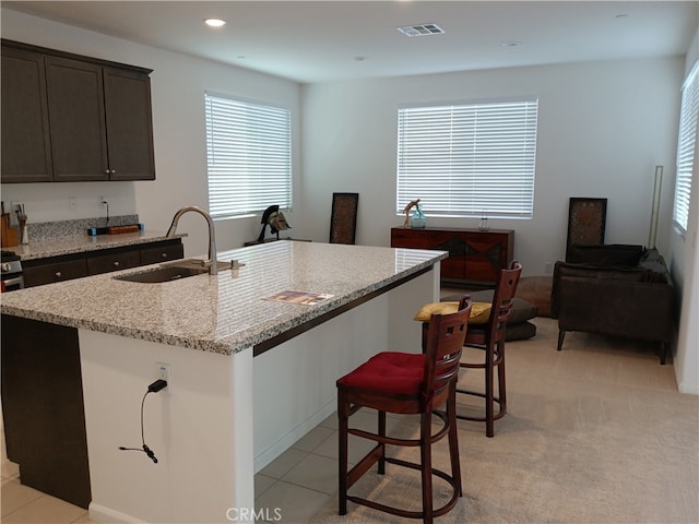 kitchen featuring light carpet, a center island with sink, sink, light stone countertops, and dark brown cabinetry