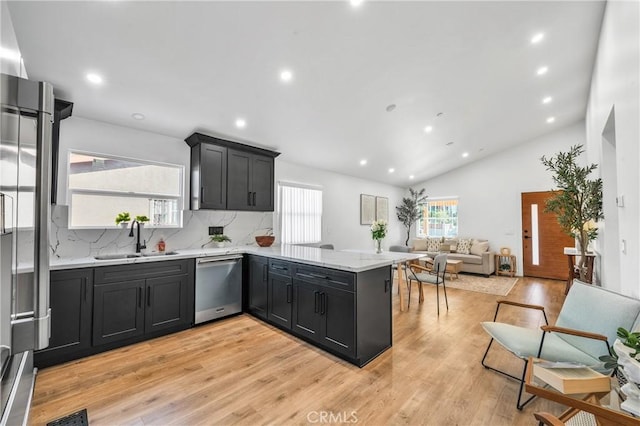 kitchen with kitchen peninsula, appliances with stainless steel finishes, vaulted ceiling, sink, and light hardwood / wood-style floors