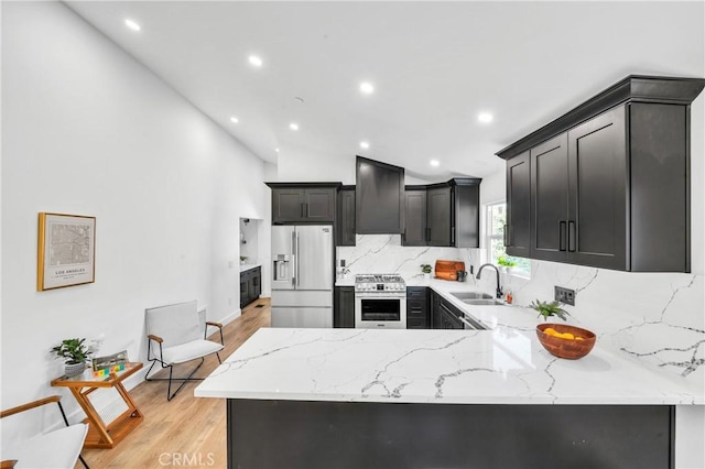 kitchen featuring vaulted ceiling, light hardwood / wood-style flooring, light stone counters, kitchen peninsula, and stainless steel appliances